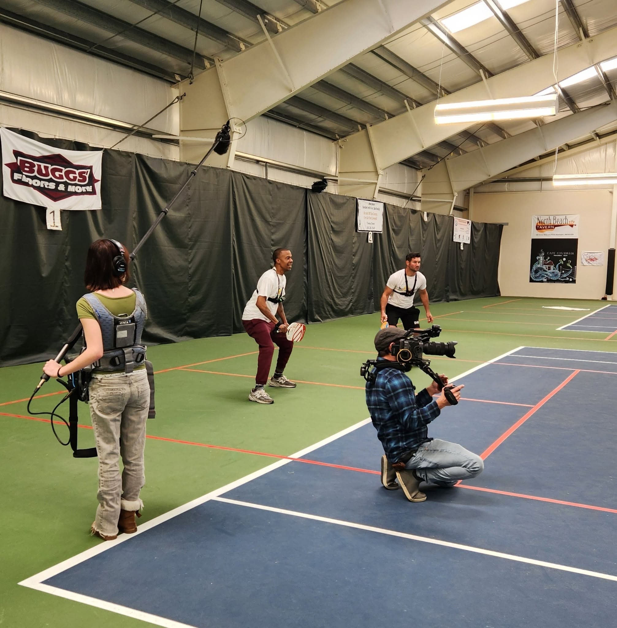 Jeremiah Rounds filming from a low camera position on a pickleball court with The Columbia Coast crew